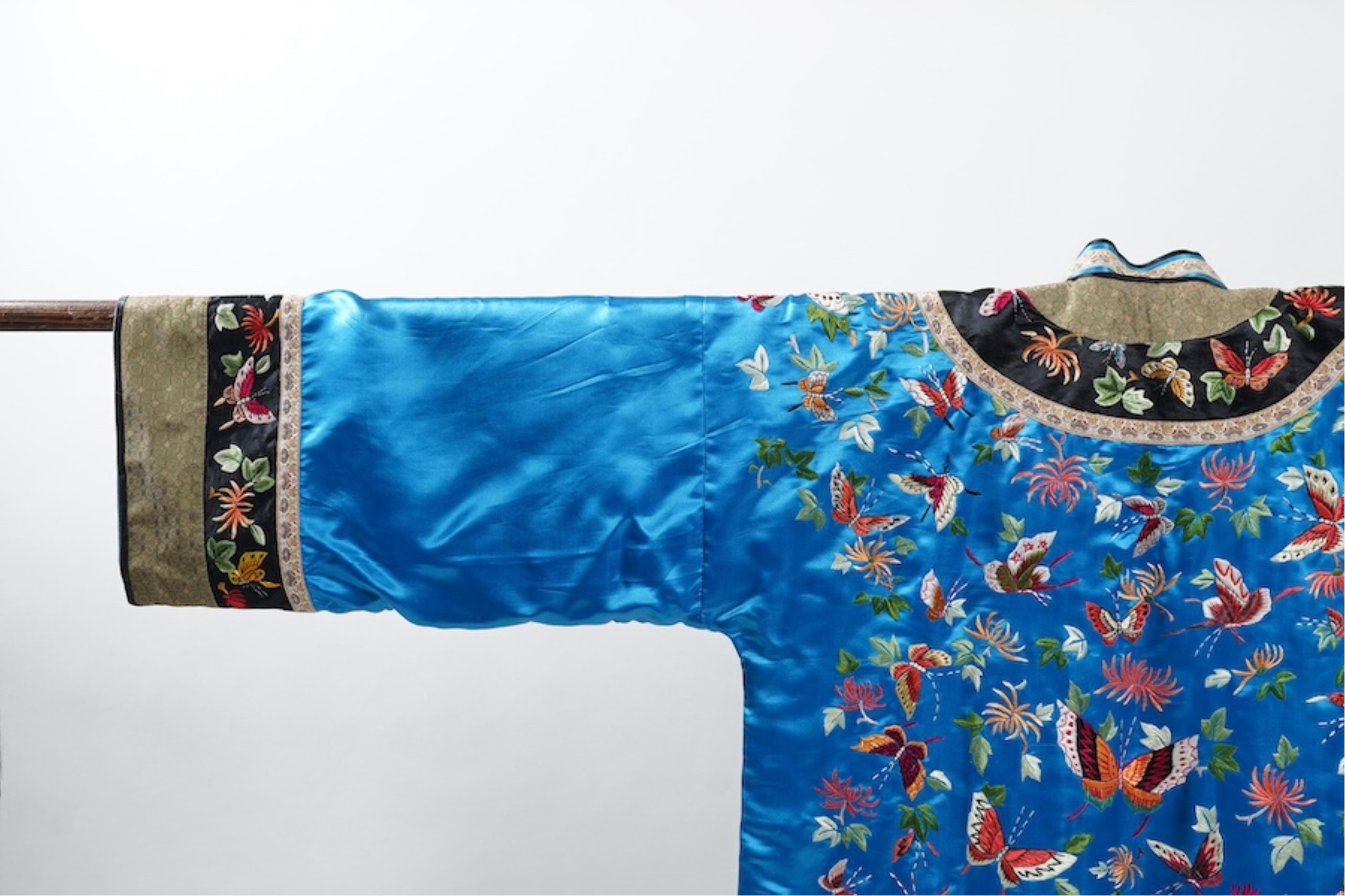 A mid 20th century Chinese turquoise silk jacket, with all over polychrome butterfly embroidery, similar embroidered sleeve bands, front and bottom edges on black silk, all bordered with gold brocade. The jacket blue sil